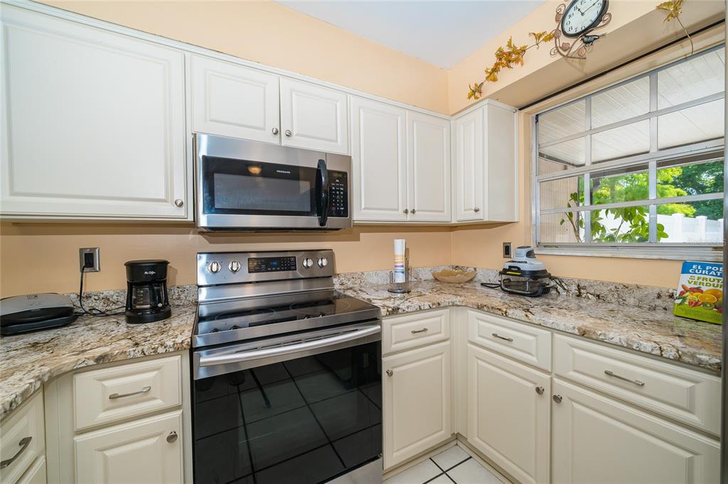 A kitchen features white cabinets, granite countertops, stainless steel appliances, and a window — 14015 LEMON VALLEY PLACE, TAMPA, FL