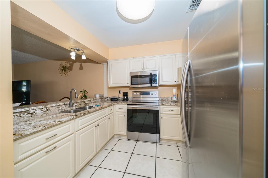 A kitchen features white cabinets, granite countertops, stainless steel appliances, and light-colored floor tiles — 14015 LEMON VALLEY PLACE, TAMPA, FL