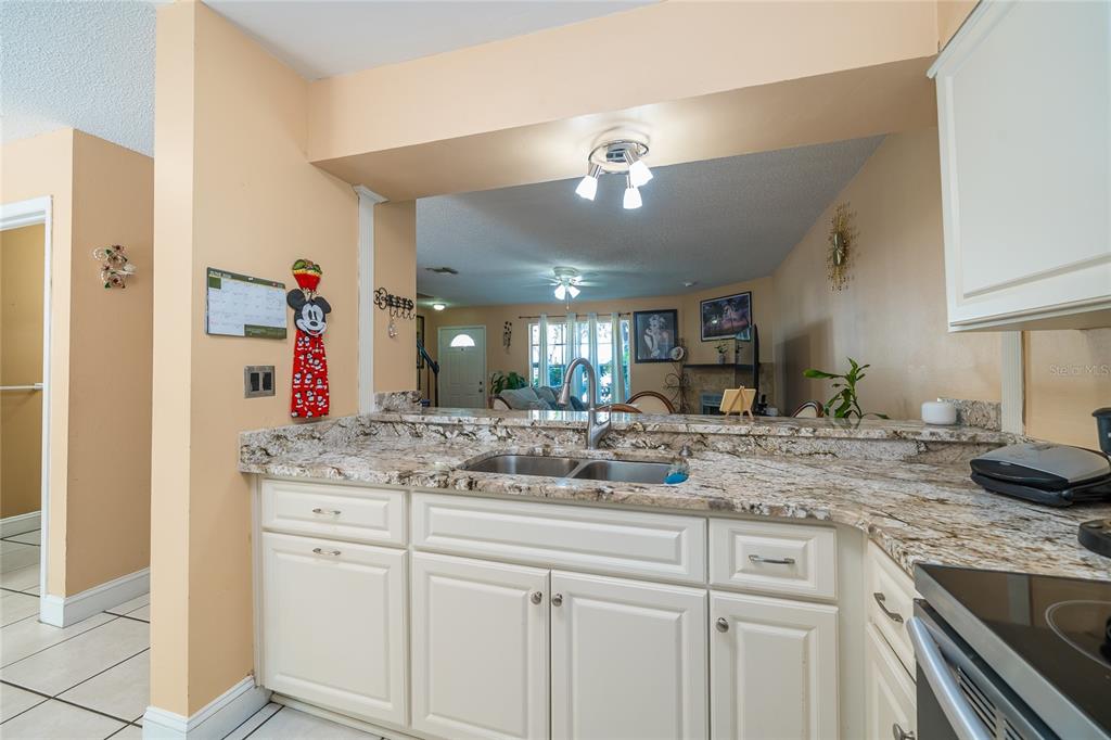 A kitchen with white cabinets and granite countertops overlooks a living area — 14015 LEMON VALLEY PLACE, TAMPA, FL