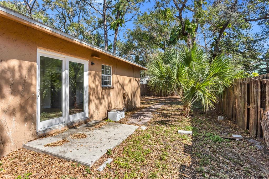A tan stucco house exterior features a concrete patio, sliding glass doors, and a window — 14717 SUNSET ST, CLEARWATER, FL