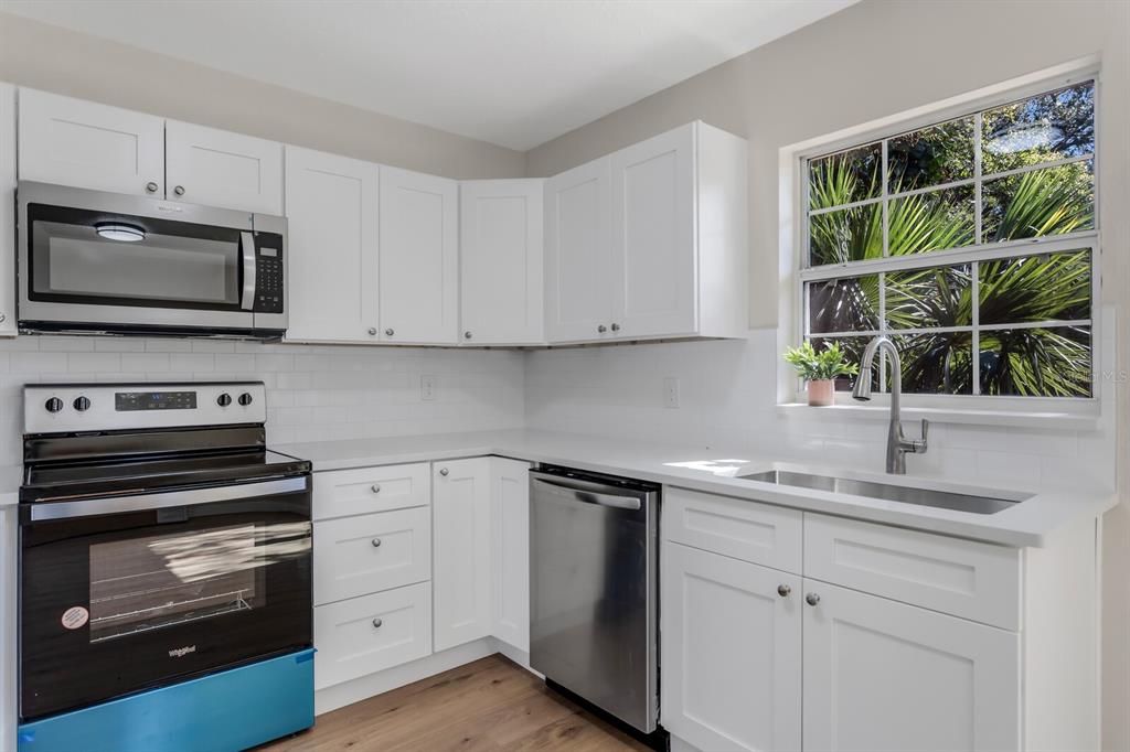 A kitchen with white cabinets, stainless steel appliances, a white subway tile backsplash, and a window — 14717 SUNSET ST, CLEARWATER, FL