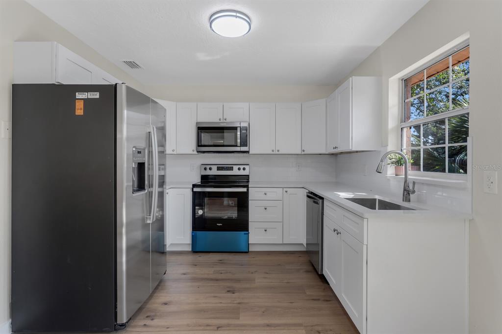 A kitchen with white cabinets, stainless steel appliances, white countertops, and wood-look flooring — 14717 SUNSET ST, CLEARWATER, FL