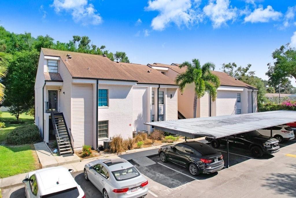 An exterior view of a multi-story apartment building with a covered parking area and cars — 4833 PURITAN CIRCLE UNIT 101, TAMPA, FL