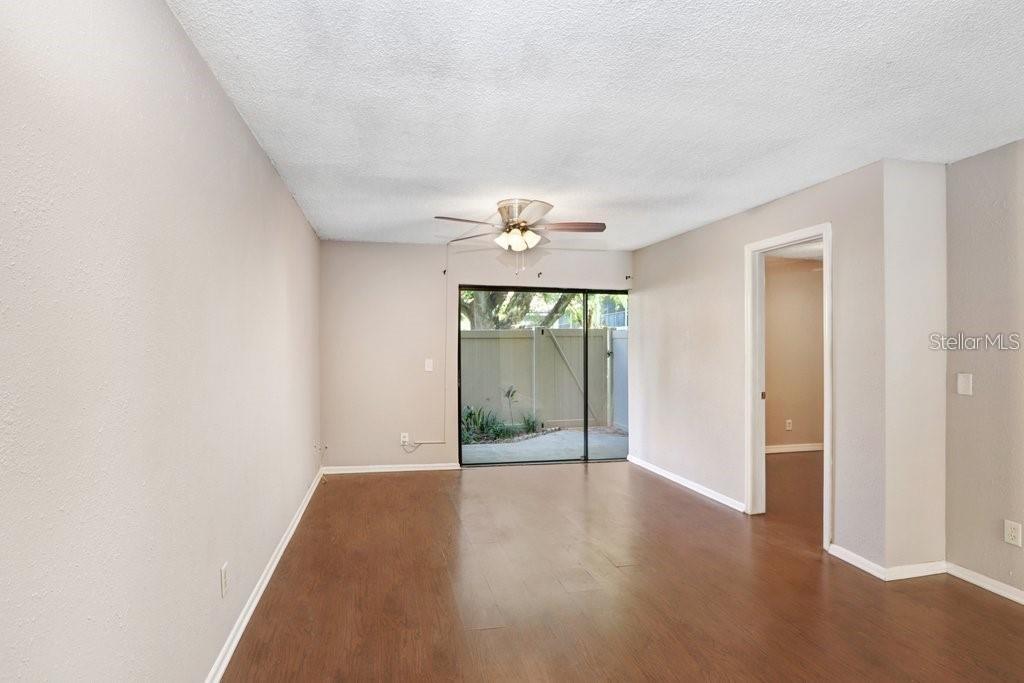 An empty living room with wood-look flooring, a ceiling fan, and a sliding glass door — 4833 PURITAN CIRCLE UNIT 101, TAMPA, FL