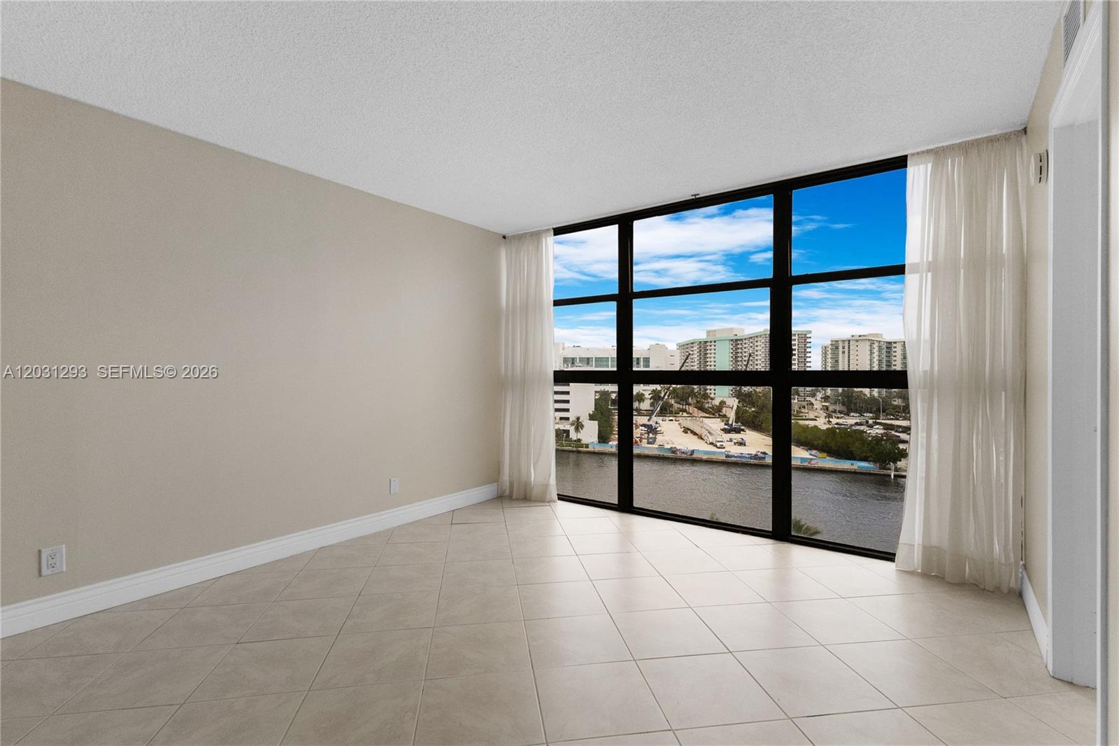 An empty room features beige tile flooring, light-colored walls, and large windows overlooking a waterway — 200 Leslie Dr # 902, Hallandale Beach FL 33009, HALLANDALE BEACH, FL
