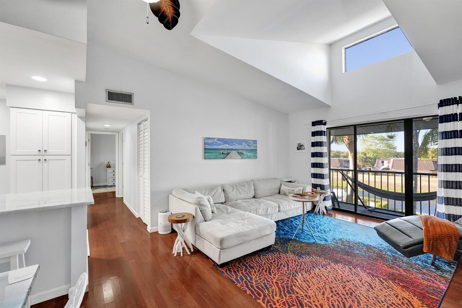 A living room features a white sectional sofa, a colorful rug, and a vaulted ceiling — 1008 Green Pine Boulevard # D3, West Palm Beach FL 33409, WEST PALM BEACH, FL