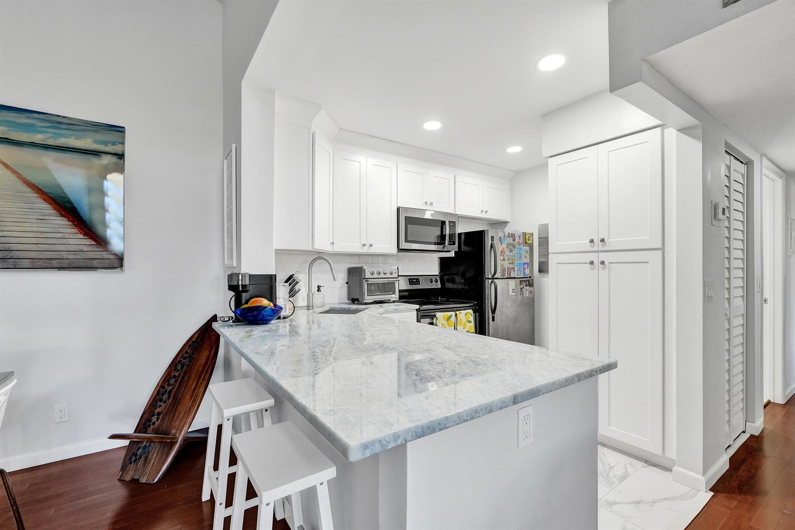 A kitchen features white cabinets, a marble-topped island with stools, and stainless steel appliances — 1008 Green Pine Boulevard # D3, West Palm Beach FL 33409, WEST PALM BEACH, FL