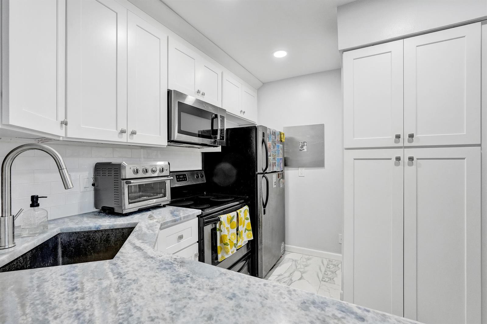 A kitchen features white cabinets, blue-toned countertops, a stainless steel microwave, and a black refrigerator — 1008 Green Pine Boulevard # D3, West Palm Beach FL 33409, WEST PALM BEACH, FL