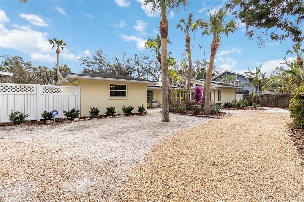 A single-story house with a gravel driveway, palm trees, and a white privacy fence — 5107 SAINT ALBANS AVENUE, SARASOTA, FL