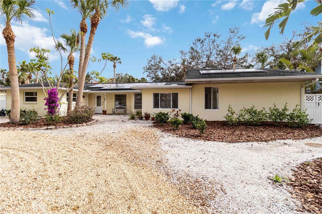 A single-story house with a gravel driveway, palm trees, and a light yellow exterior — 5107 SAINT ALBANS AVENUE, SARASOTA, FL