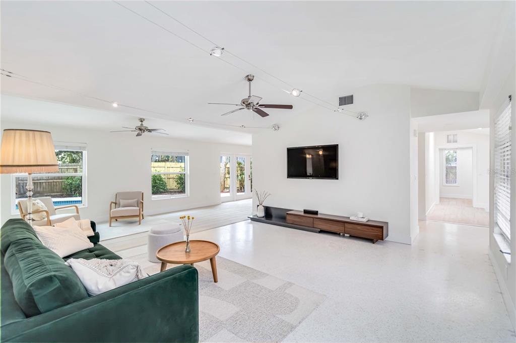 A bright living room features a green sofa, a wall-mounted television, and white tile floors — 5107 SAINT ALBANS AVENUE, SARASOTA, FL