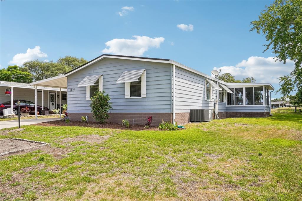 A light blue single-story house with a carport, brick skirting, and a screened-in porch — 1616 W SCHWARTZ BOULEVARD, LADY LAKE, FL