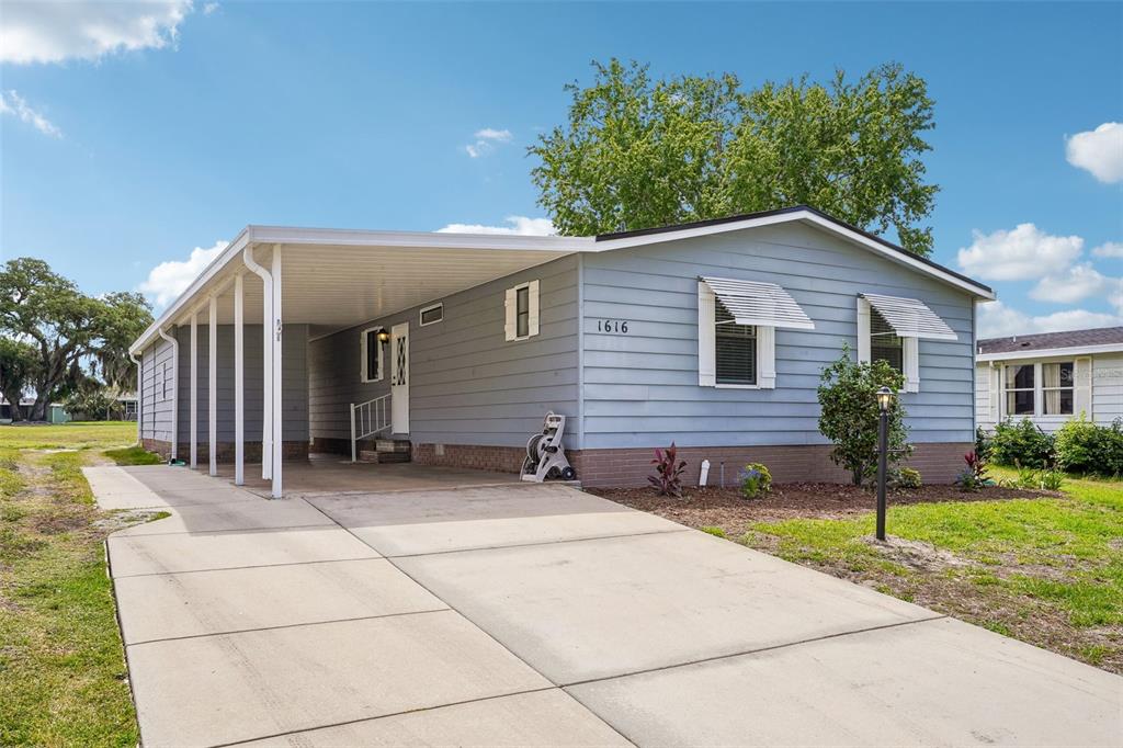 A light blue single-story house features a concrete driveway, a carport, and white window awnings — 1616 W SCHWARTZ BOULEVARD, LADY LAKE, FL