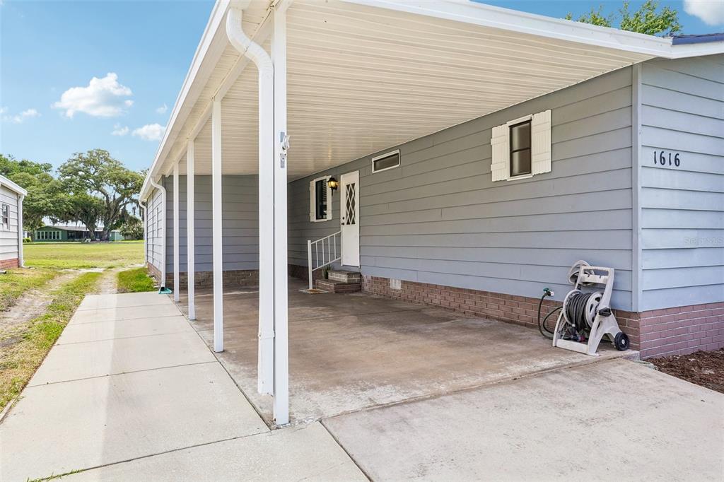 A gray house exterior features a concrete carport, a white door, and a hose reel — 1616 W SCHWARTZ BOULEVARD, LADY LAKE, FL