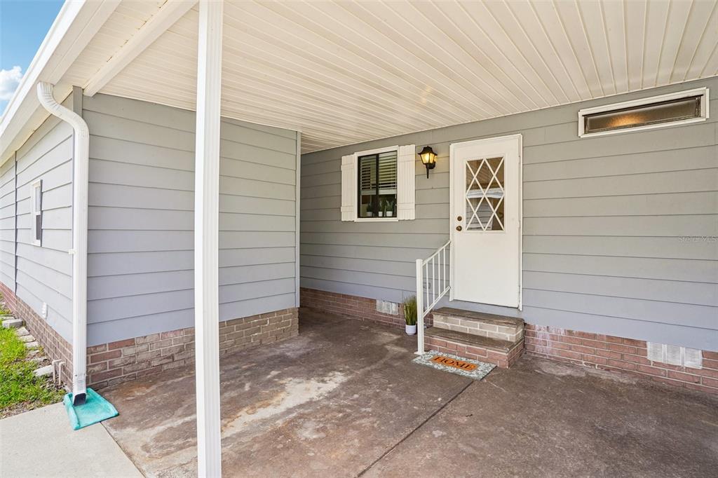 A covered concrete porch leads to a white front door on a gray-sided house — 1616 W SCHWARTZ BOULEVARD, LADY LAKE, FL
