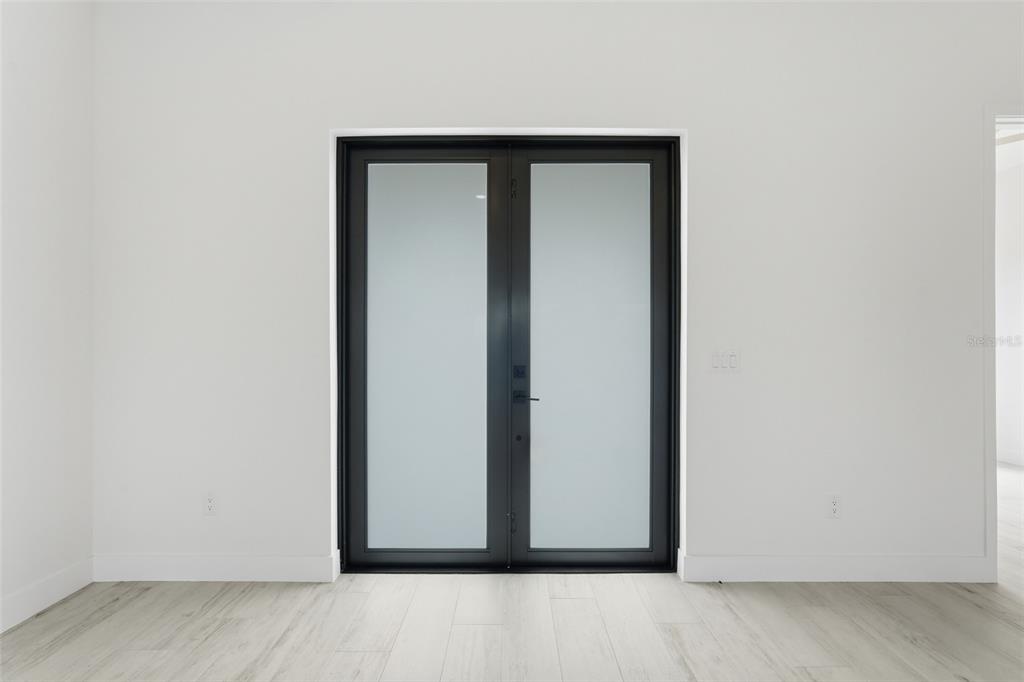 A room with light wood-look flooring and white walls features a black-framed double glass door — 8472 AGATE STREET, PORT CHARLOTTE, FL