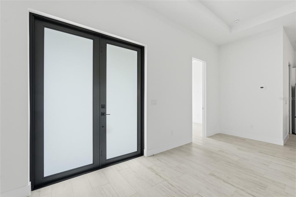 A bright room features light wood-look flooring, white walls, and a set of black-framed glass doors — 8472 AGATE STREET, PORT CHARLOTTE, FL