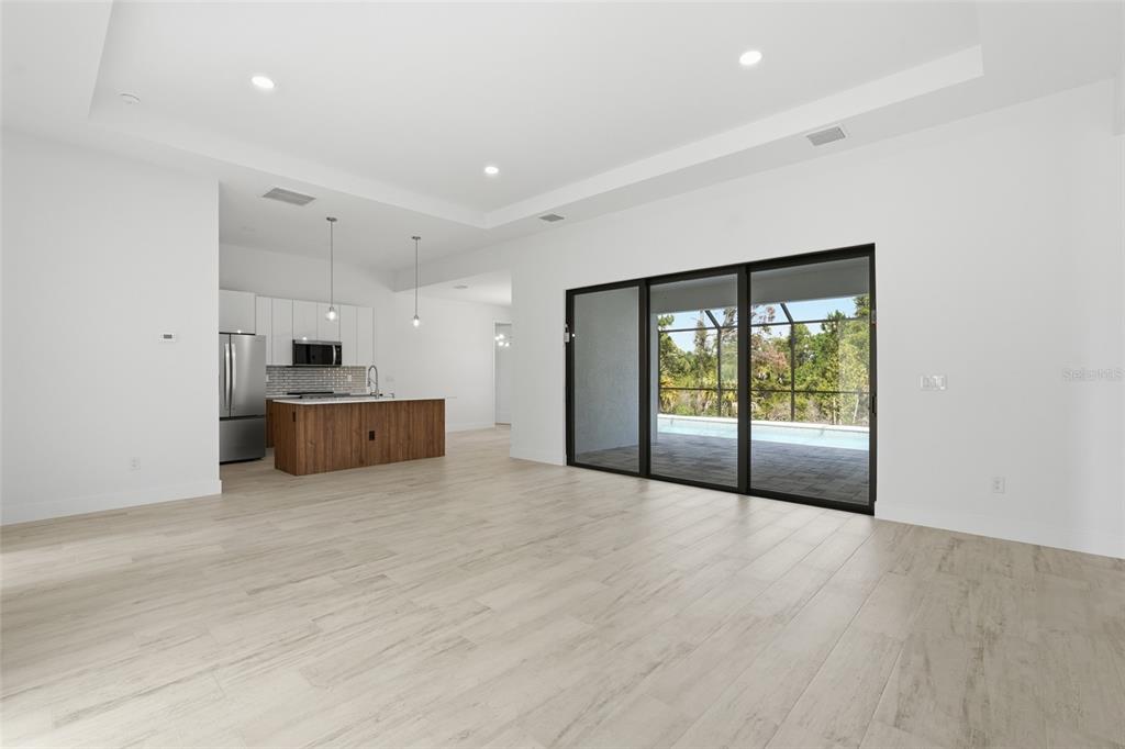 A bright, open-concept living area features light wood-look tile flooring, a kitchen island, and sliding doors — 8472 AGATE STREET, PORT CHARLOTTE, FL