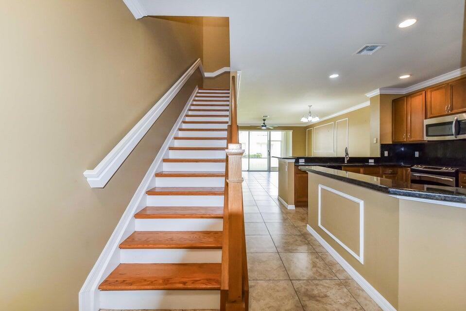 A staircase with wooden treads and white risers sits beside a kitchen with dark cabinets — 9687 Lago Drive, Boynton Beach FL 33472, BOYNTON BEACH, FL