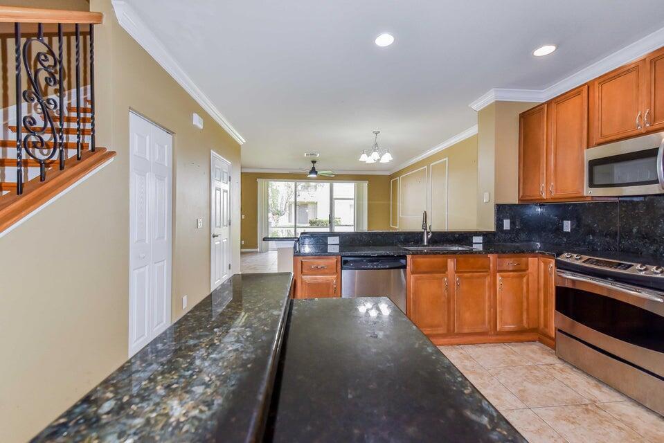 A kitchen with dark granite countertops, wooden cabinets, and stainless steel appliances overlooks a living area — 9687 Lago Drive, Boynton Beach FL 33472, BOYNTON BEACH, FL
