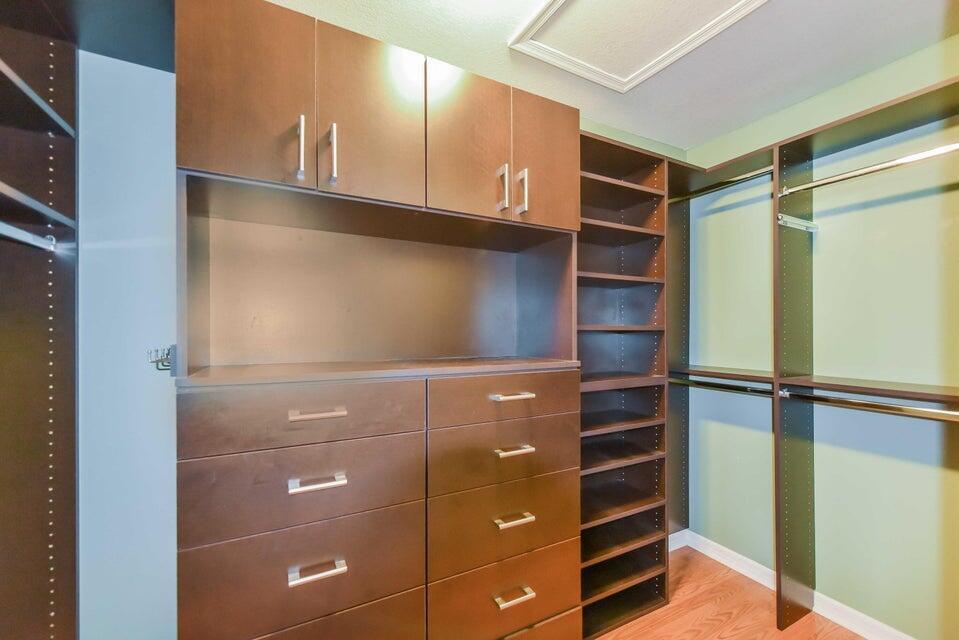 A walk-in closet features dark wood cabinetry, built-in shelving, drawers, and hanging rods — 9687 Lago Drive, Boynton Beach FL 33472, BOYNTON BEACH, FL