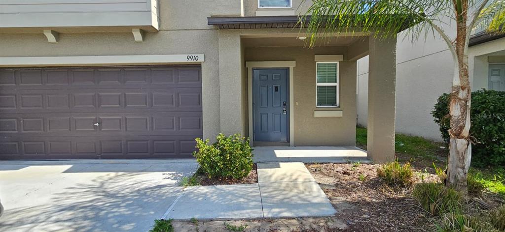 A two-story house exterior features a gray garage door, a blue front door, and landscaping — 9910 SPANISH LIME COURT, RIVERVIEW, FL