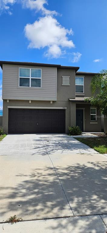 A two-story house features a brown garage, beige stucco siding, and a concrete driveway — 9910 SPANISH LIME COURT, RIVERVIEW, FL