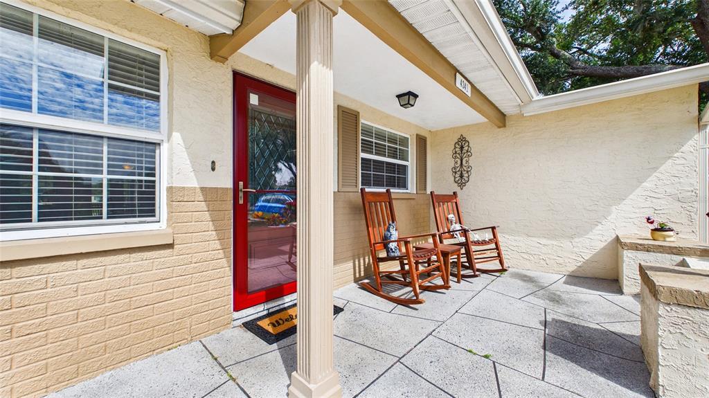 A covered front porch features a red door, two wooden rocking chairs, and stone flooring — 4341 OTTER WAY, NEW PORT RICHEY, FL