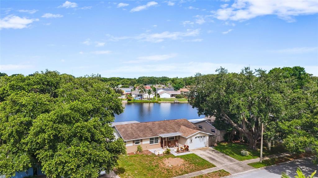 An aerial view shows a single-story house with a brown roof situated beside a lake — 4341 OTTER WAY, NEW PORT RICHEY, FL