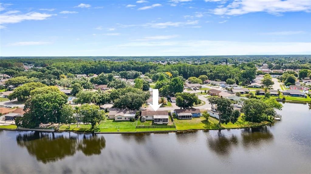 An aerial view shows a single-story house with a screened porch situated along a lake — 4341 OTTER WAY, NEW PORT RICHEY, FL