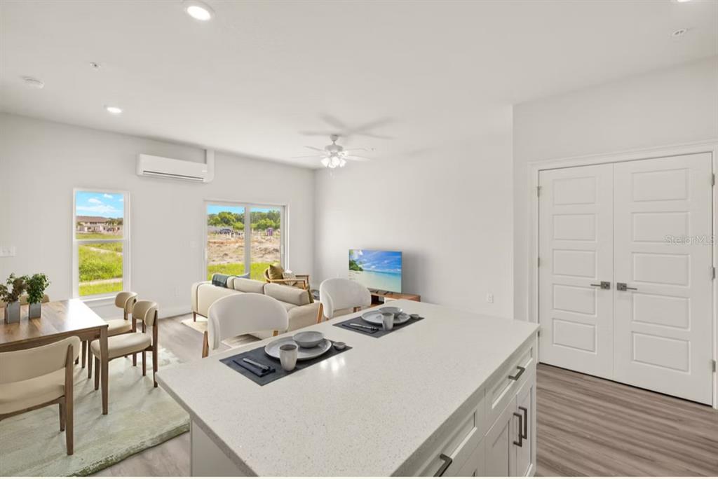 A kitchen island overlooks a living and dining area with white walls and light flooring — 14987 SUNSET EVE LOOP, FORT MYERS, FL