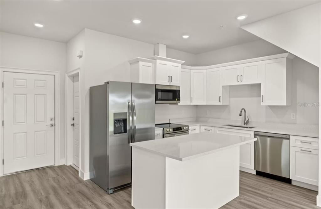 A kitchen features white cabinets, stainless steel appliances, a center island, and wood-look flooring — 14987 SUNSET EVE LOOP, FORT MYERS, FL