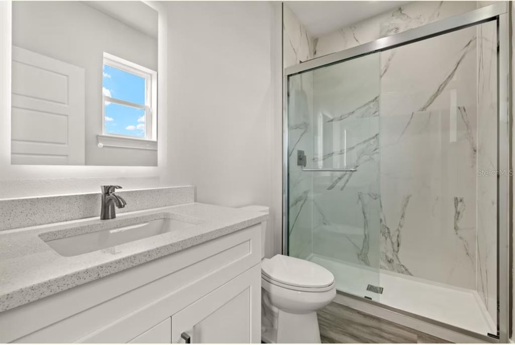 A modern bathroom features a white vanity, a toilet, and a glass-enclosed marble-tiled shower — 14987 SUNSET EVE LOOP, FORT MYERS, FL