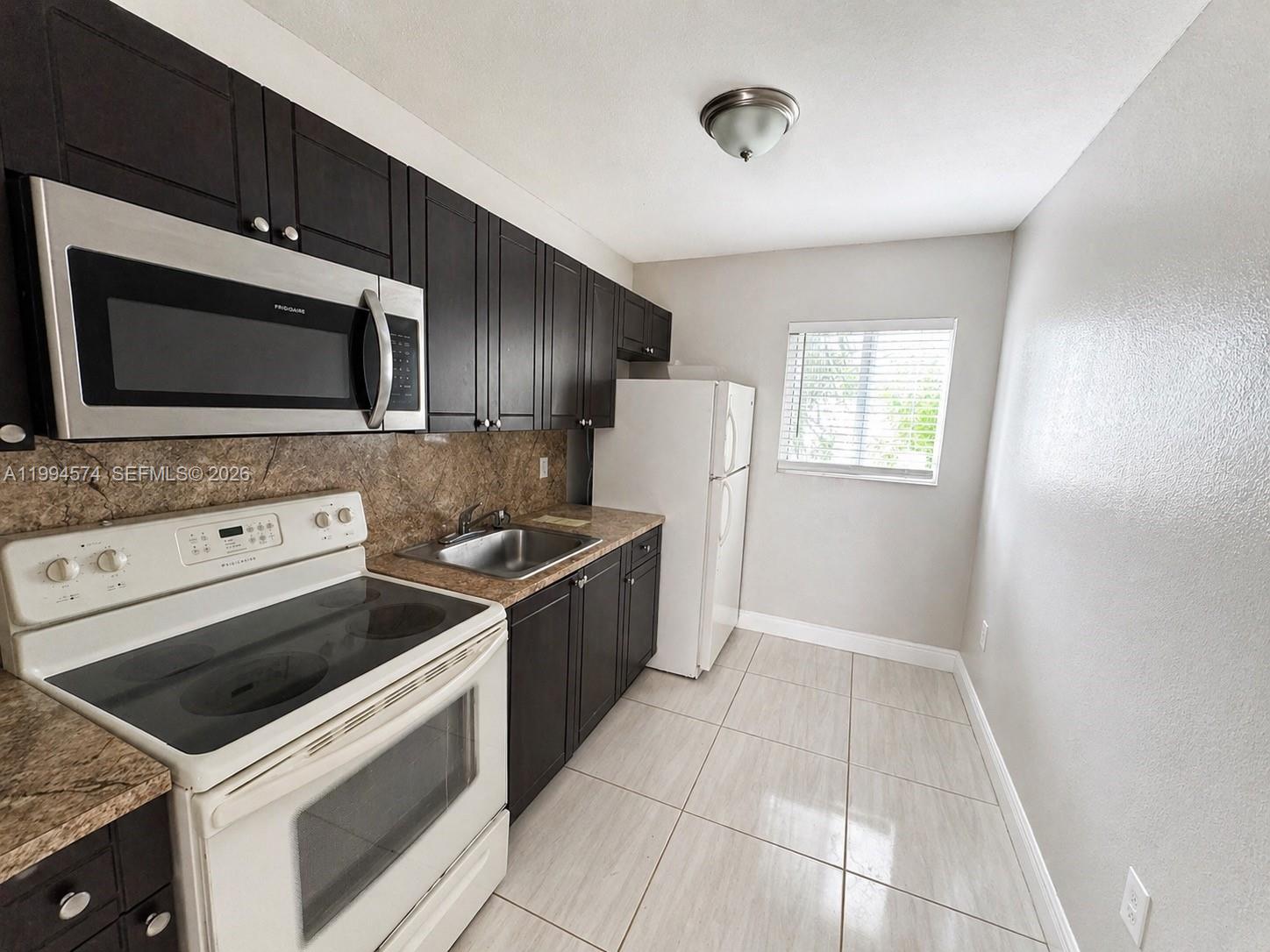 A kitchen features dark wood cabinets, stainless steel appliances, a white stove, and tile flooring — 1920 Washington Ave # 3, Opa-Locka FL 33054, OPA-LOCKA, FL