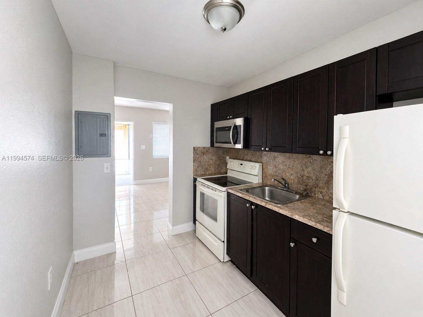 A kitchen features dark wood cabinets, white appliances, and light tile flooring — 1920 Washington Ave # 3, Opa-Locka FL 33054, OPA-LOCKA, FL
