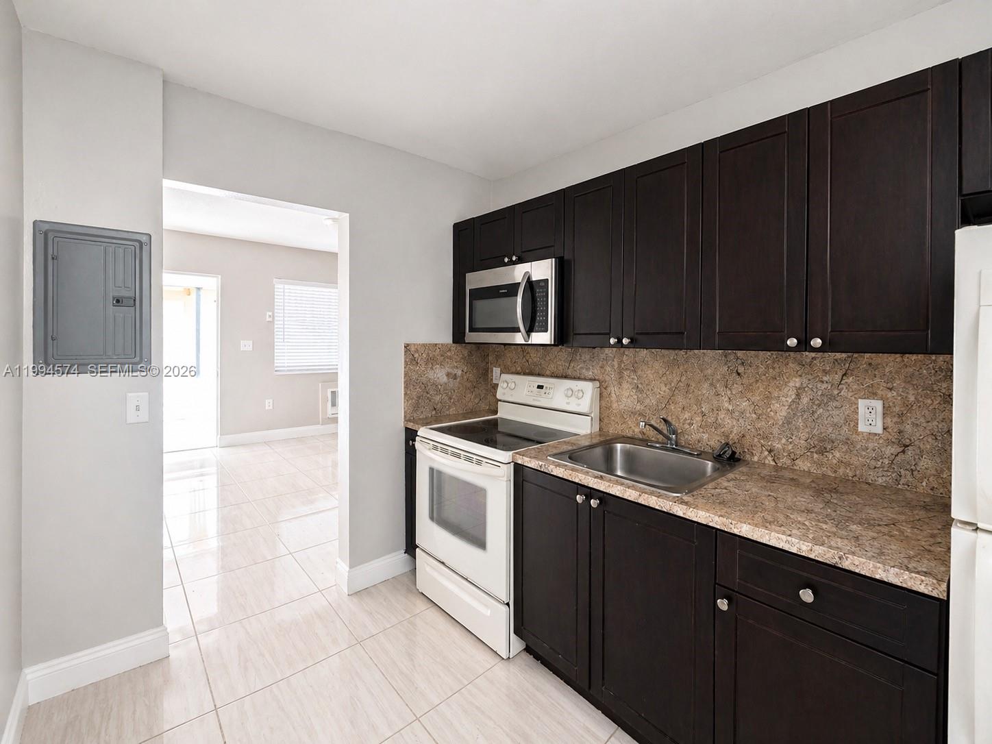 A kitchen features dark wood cabinets, a white stove, and a brown stone-patterned backsplash — 1920 Washington Ave # 3, Opa-Locka FL 33054, OPA-LOCKA, FL