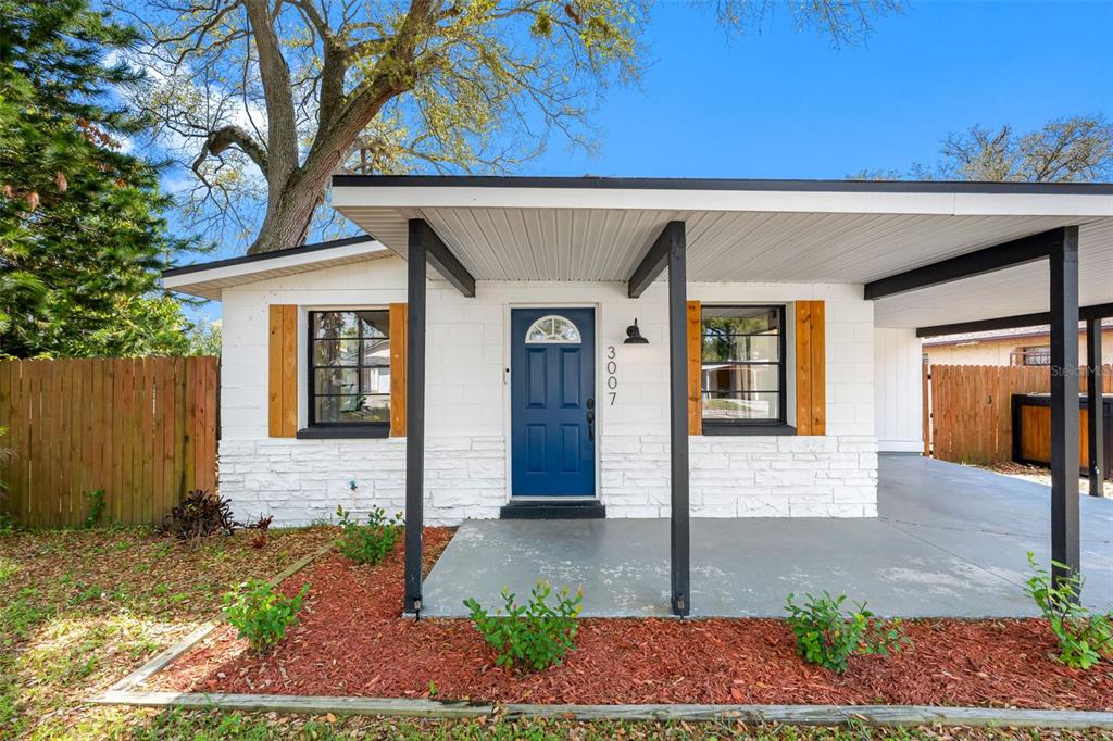 A single-story house features a white brick exterior, a blue front door, and a carport — 3007 CHIPCO STREET, TAMPA, FL