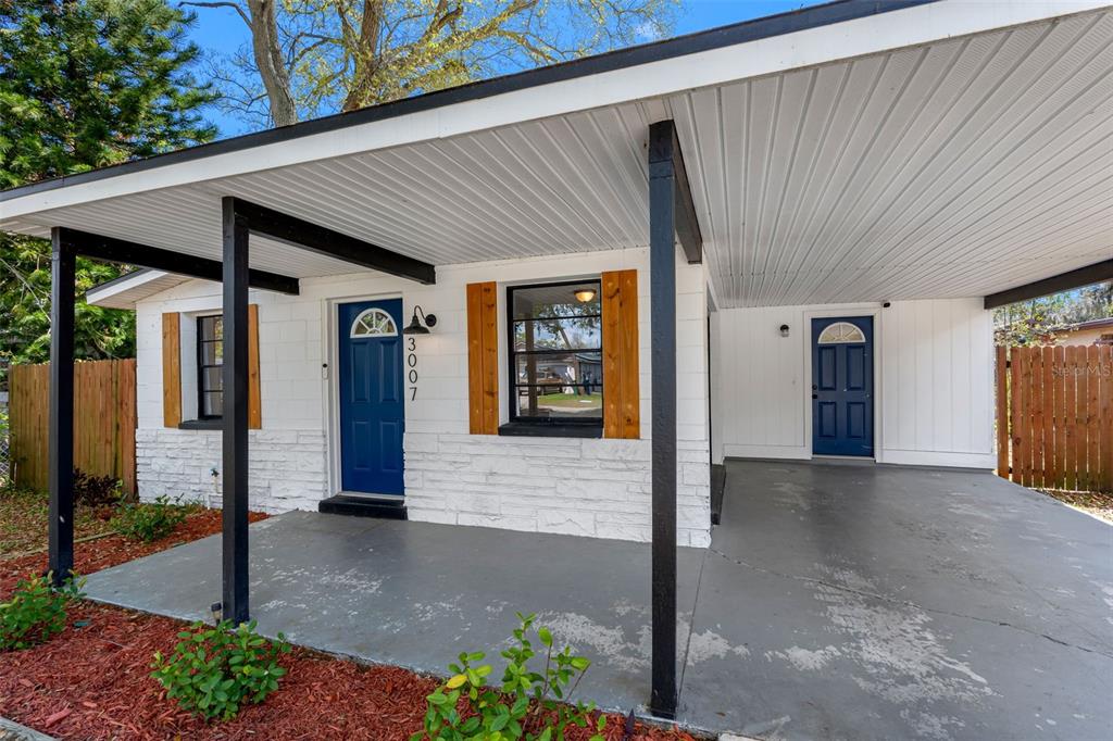 A white house exterior features a carport, two blue doors, and wood-accented windows — 3007 CHIPCO STREET, TAMPA, FL