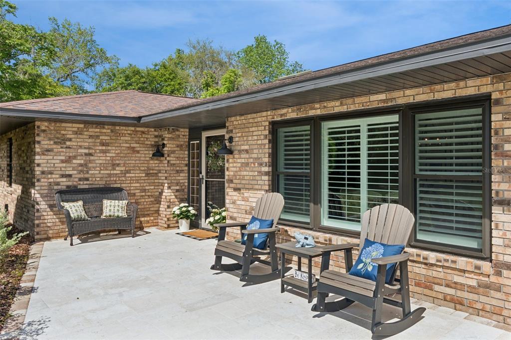 A brick house exterior features a light-colored patio with rocking chairs and a wicker bench — 1908 POPPY LANE, PORT ORANGE, FL