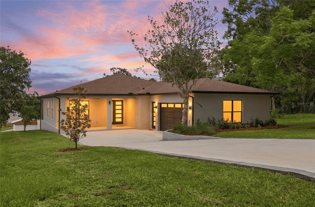 A single-story house with a concrete driveway, brown roof, and tan exterior at dusk — 17540 THIRD STREET, MONTVERDE, FL