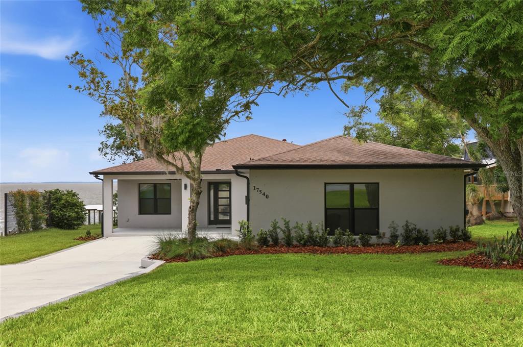 A single-story house with a gray exterior, dark-framed windows, and a concrete driveway near water — 17540 THIRD STREET, MONTVERDE, FL