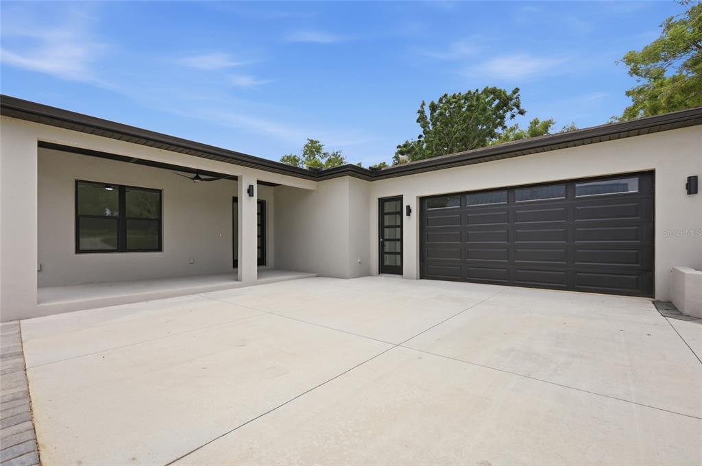 A modern house exterior features a concrete driveway, a covered patio, and a dark garage door — 17540 THIRD STREET, MONTVERDE, FL