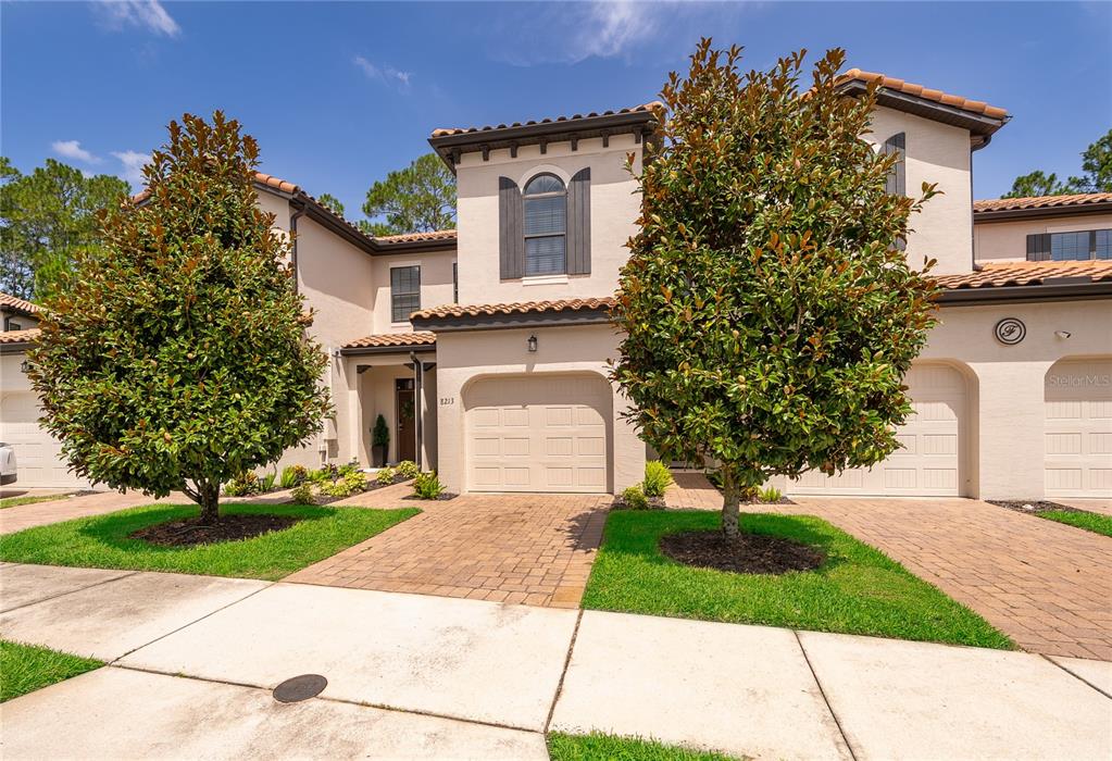 A two-story stucco townhouse with a tile roof, two garage doors, and two large trees — 8213 ROSEVILLE BOULEVARD, DAVENPORT, FL