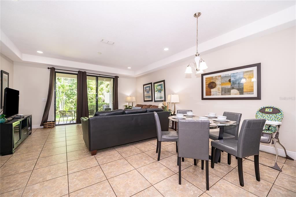 An open-concept living and dining area features tile flooring, a leather sofa, and sliding doors — 8213 ROSEVILLE BOULEVARD, DAVENPORT, FL