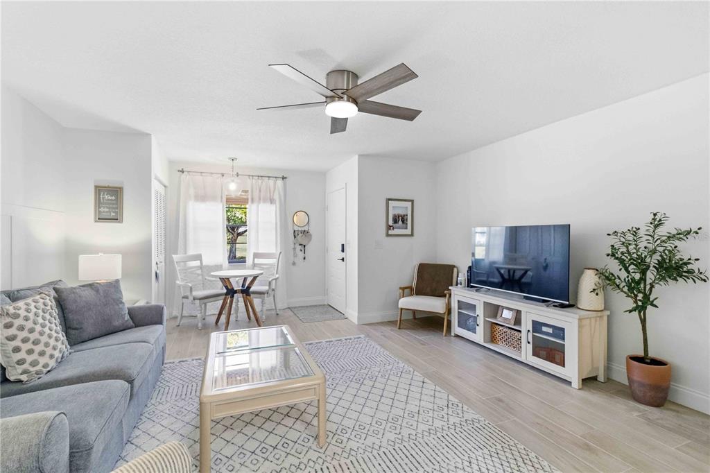 A living room features light wood-look flooring, a grey sofa, a television console, and a ceiling fan — 4237 66TH STREET CIRCLE W UNIT S-4237, BRADENTON, FL