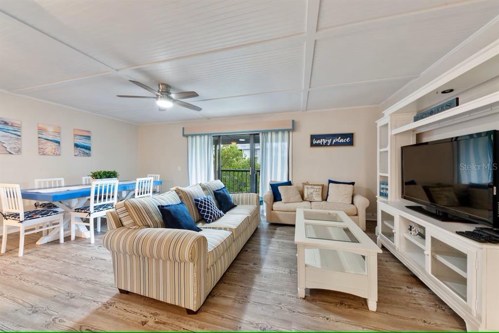 A living and dining area features striped furniture, a white media console, and wood-look flooring — 19823 GULF BOULEVARD UNIT 42, INDIAN SHORES, FL