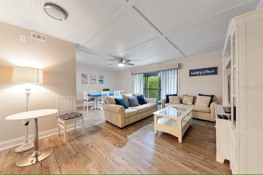 A living room and dining area feature wood-look flooring, a striped sofa, and white furniture — 19823 GULF BOULEVARD UNIT 42, INDIAN SHORES, FL