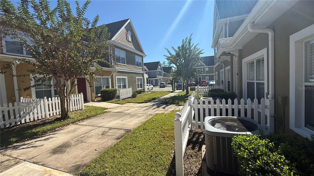 A view of a residential walkway between two-story townhomes with white picket fences — 4563 YELLOWGOLD ROAD E UNIT 106, KISSIMMEE, FL
