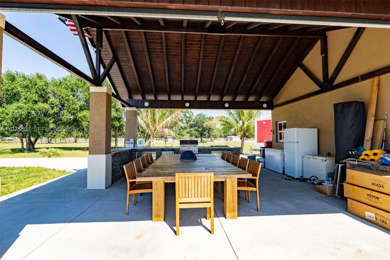 A covered outdoor patio features a large wooden dining table, chairs, and kitchen appliances — 21810 NW 270TH ST, Okeechobee FL 34972, OKEECHOBEE, FL
