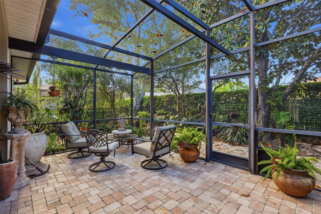 A screened-in patio features paver flooring, outdoor furniture, and various potted plants — 1609 VICTORIA GARDENS DRIVE, DELAND, FL